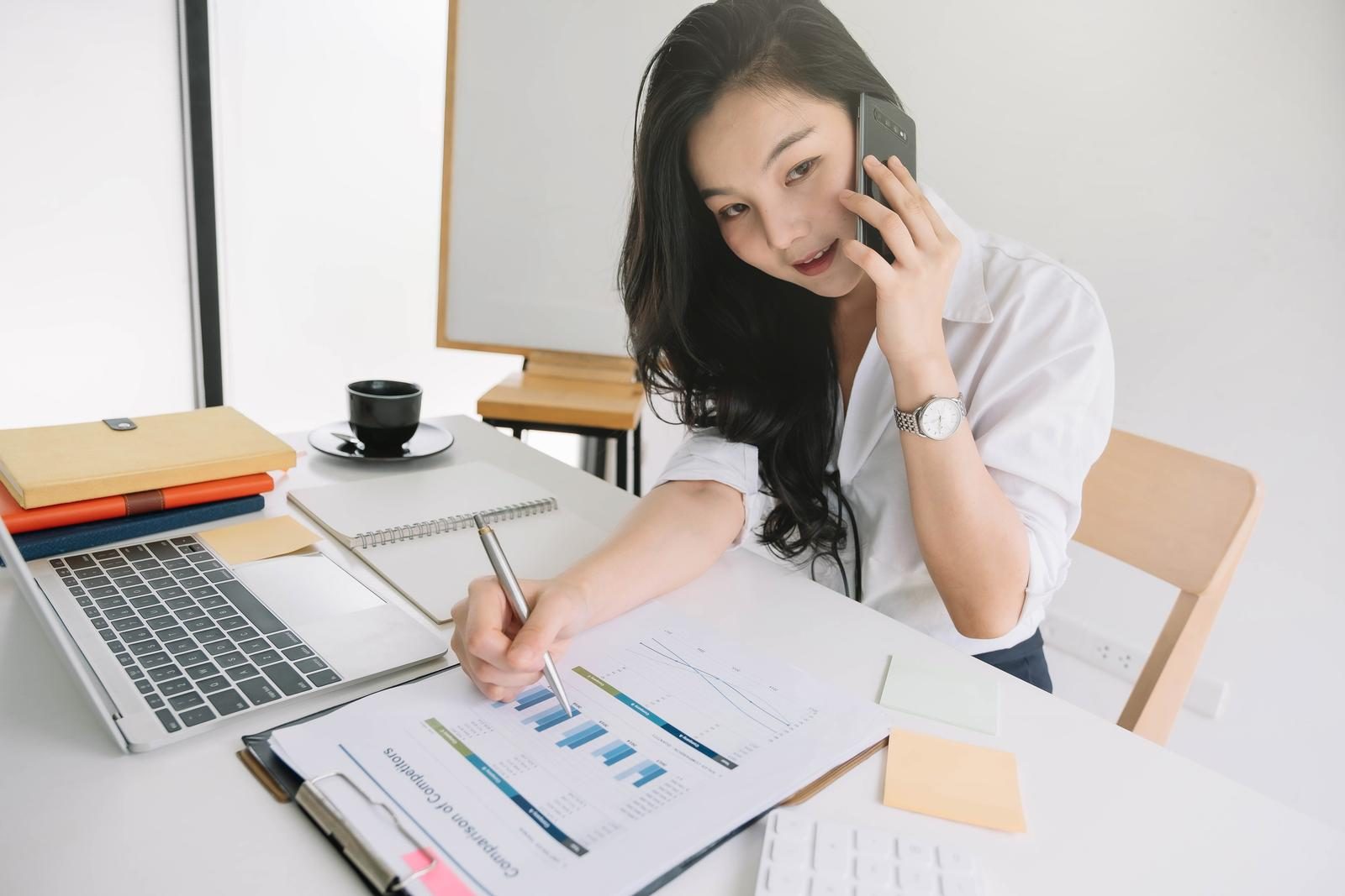 Mujer que habla por teléfono y revisa gráficas en su escritorio