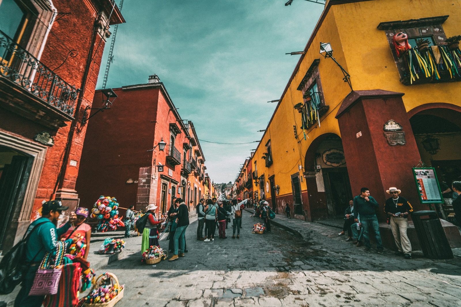 Calle empedrada de un pueblo colonial con fachadas de colores y una vendedora de artesanías