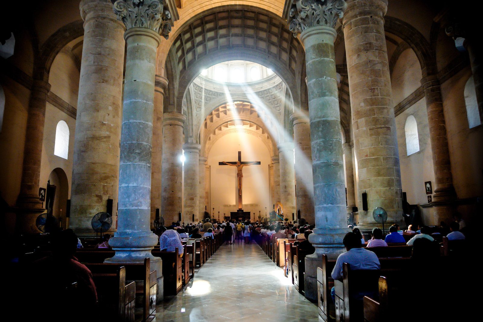 Interior de una catedral con columnas de piedra y rayos de luz sobre el altar