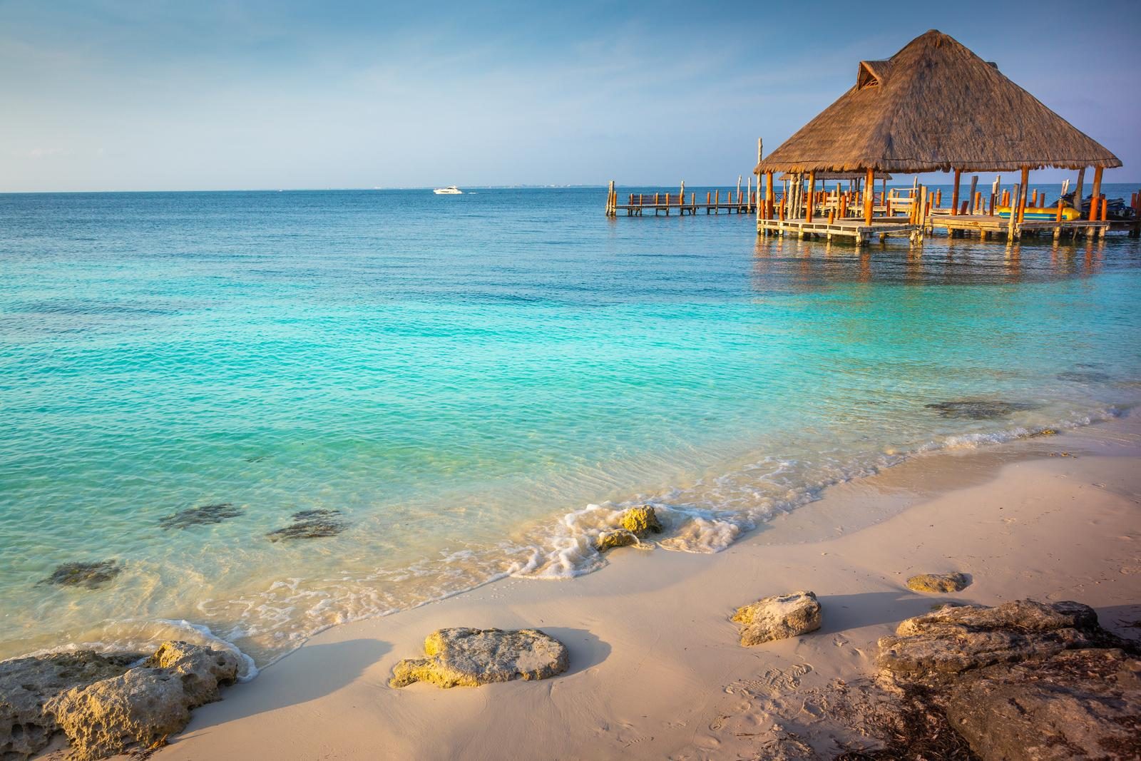 Palapa sobre un muelle en una playa de agua turquesa al atardecer