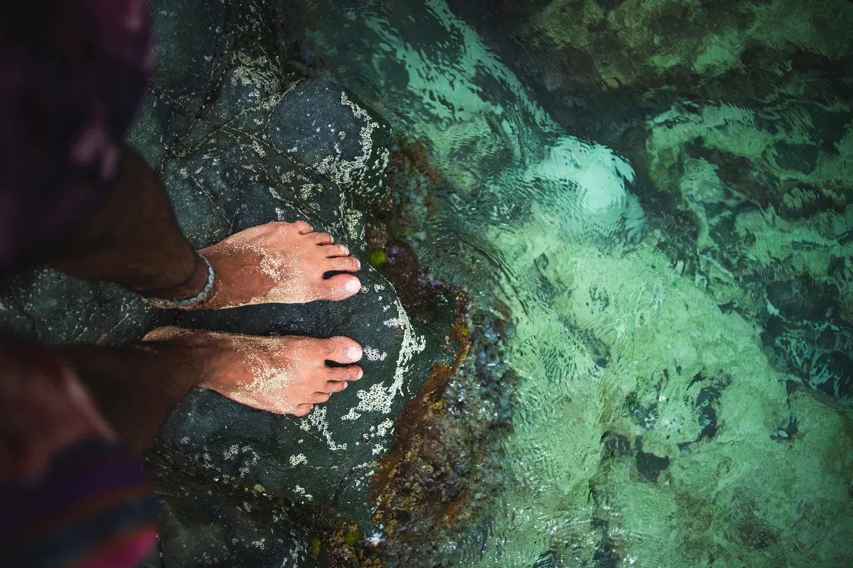 Persona parada en la orilla rocosa de un cenote de agua cristalina