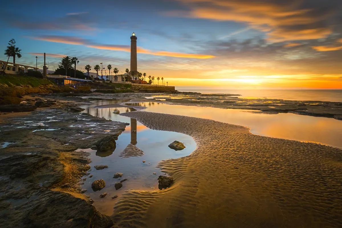 Faro junto a pozas de marea al atardecer en una costa rocosa