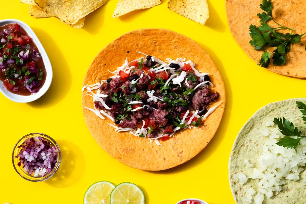 Tortilla con carne, salsas y cilantro sobre un fondo amarillo