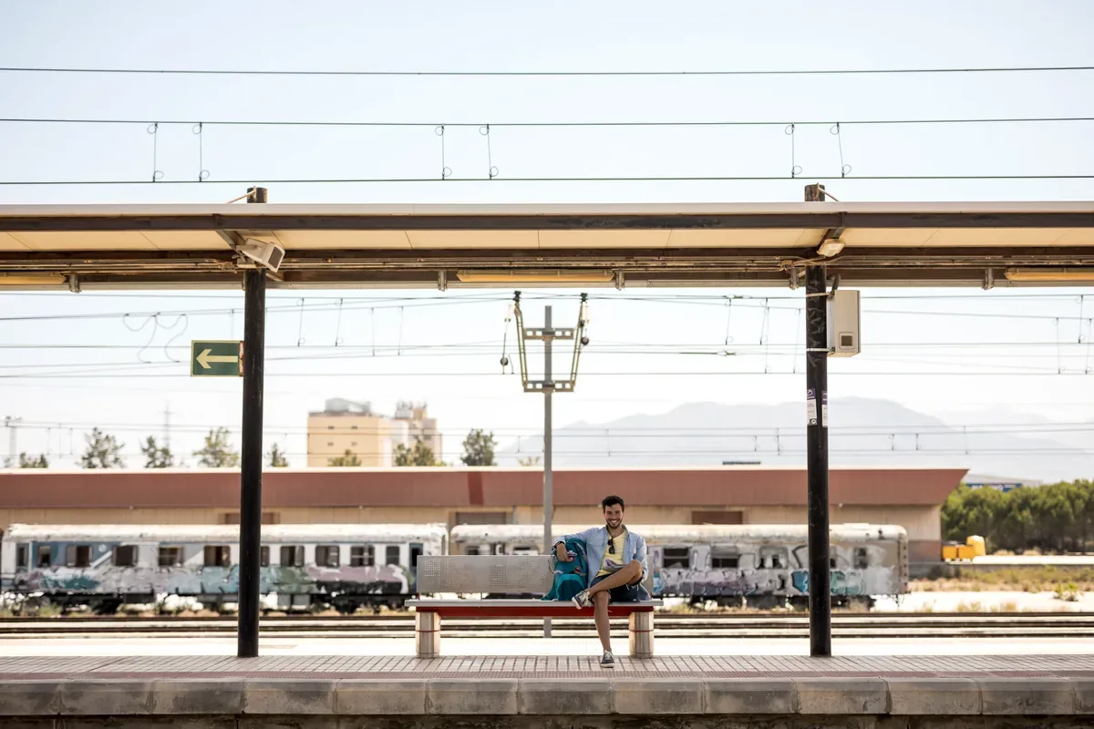 Pasajero sentado en el andén de una estación de tren frente a un vagón