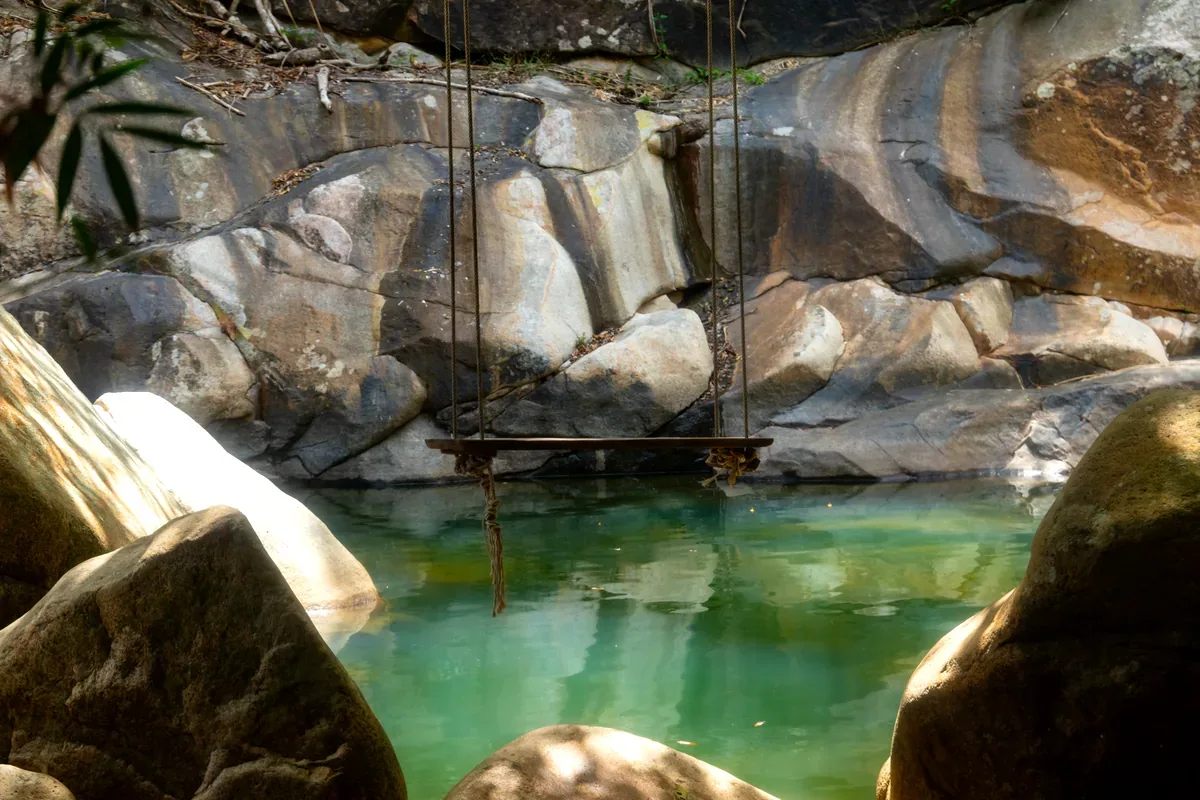 Poza de agua verde entre grandes rocas con un columpio de madera colgado