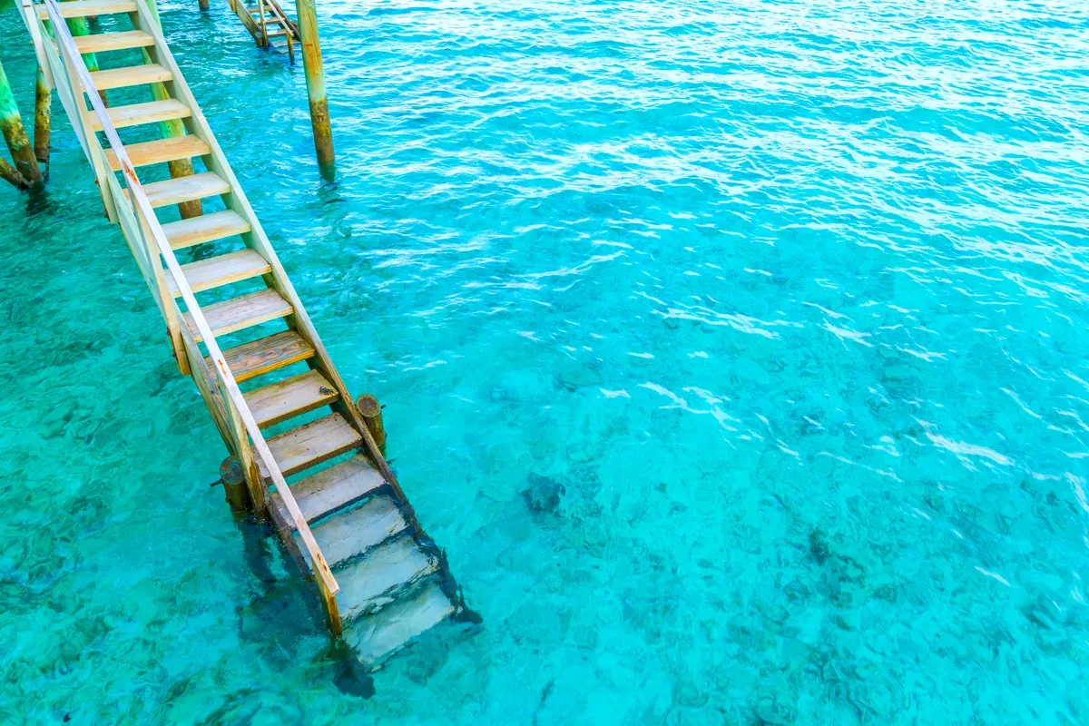 Escalera de madera que baja a un mar turquesa transparente