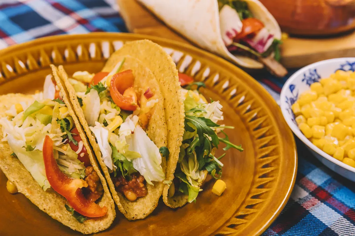 Tacos de tortilla dorada con verduras y salsa junto a un plato con elote