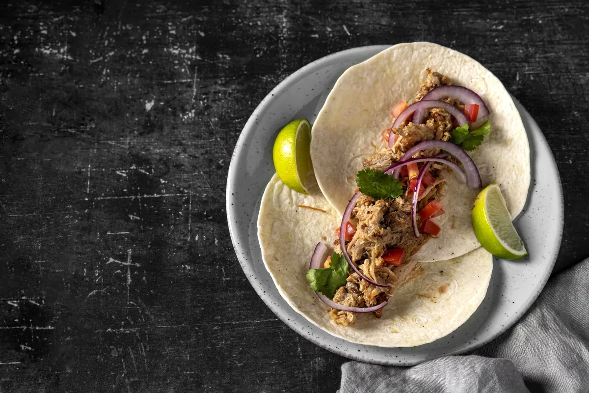 Taco con carne deshebrada, cebolla morada y limón en un plato sobre fondo oscuro