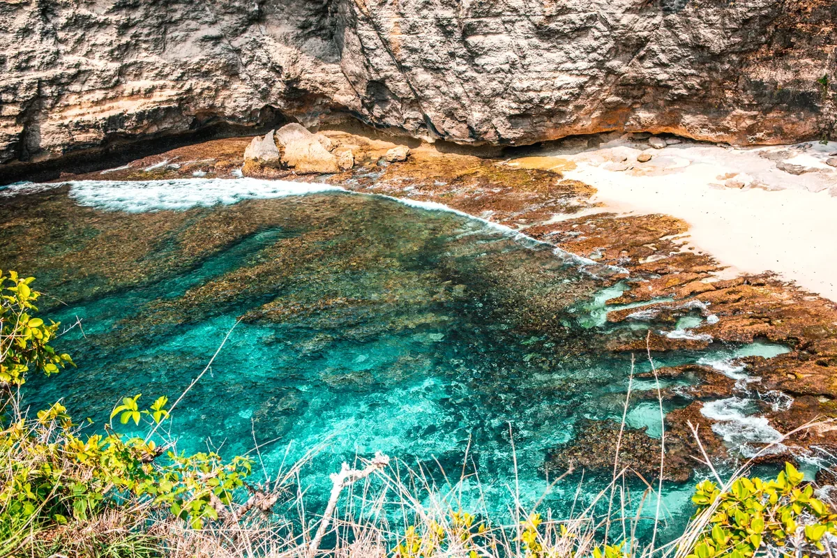 Pozas de agua turquesa entre rocas y arena bajo un acantilado