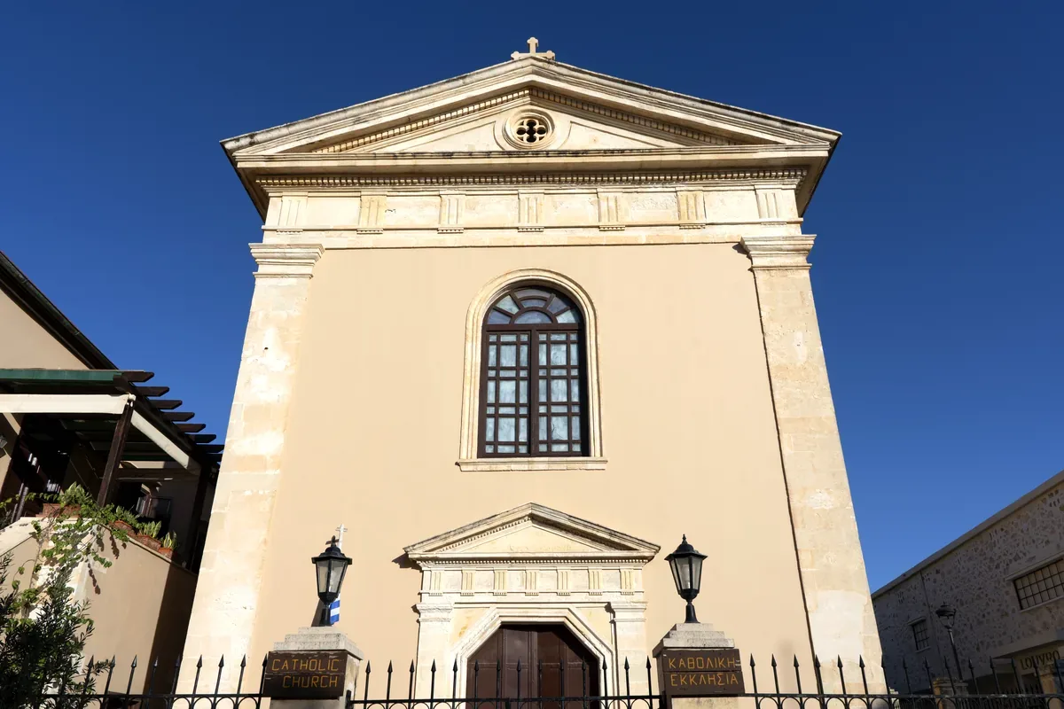 Fachada clásica de una iglesia de color crema bajo un cielo azul