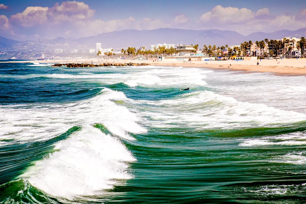 Olas grandes que rompen frente a una playa con edificios y montañas
