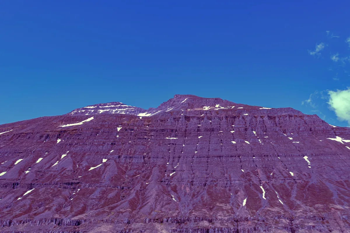 Montaña de laderas violáceas con manchas de nieve bajo un cielo azul