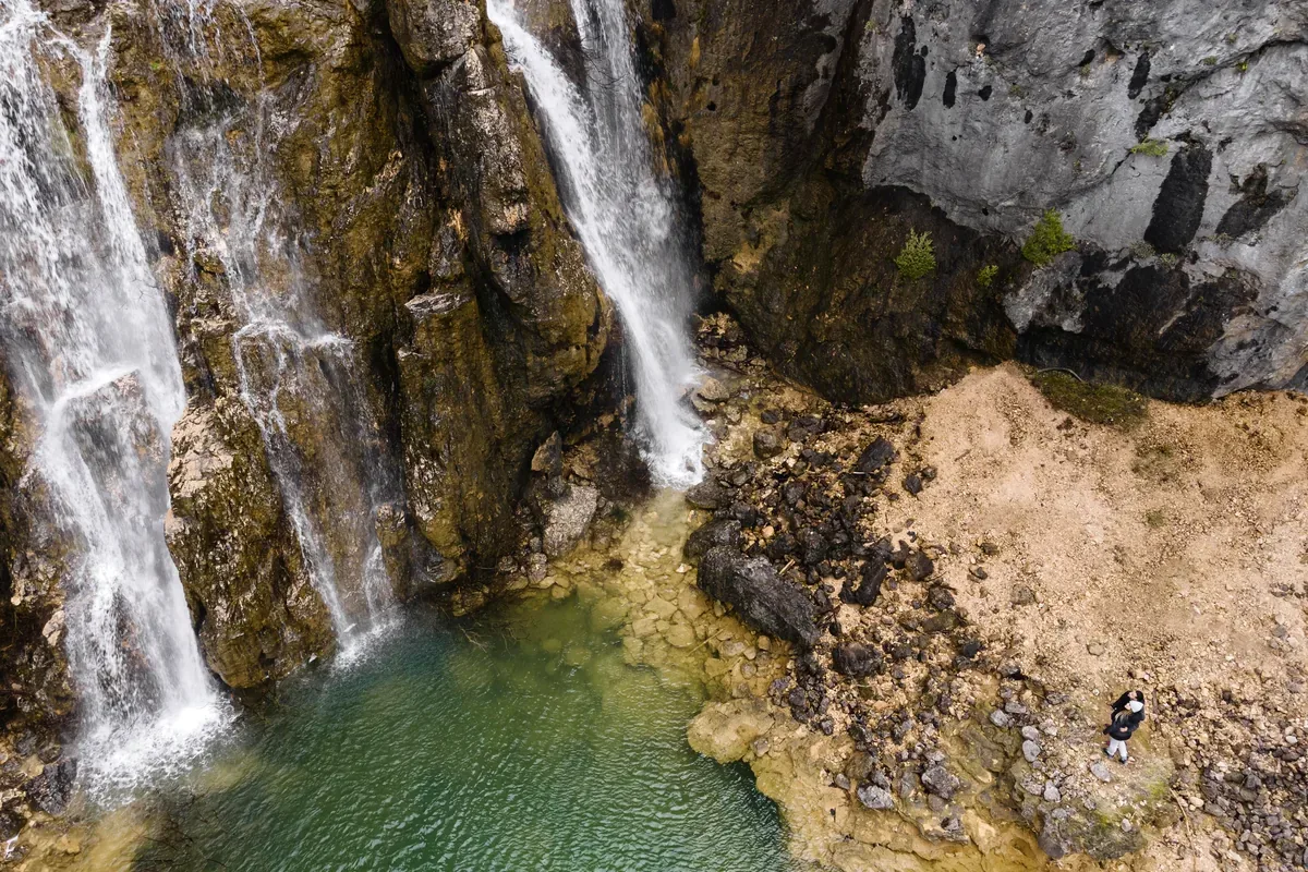 Cascadas que caen por paredes de roca a una poza verde, vistas desde arriba