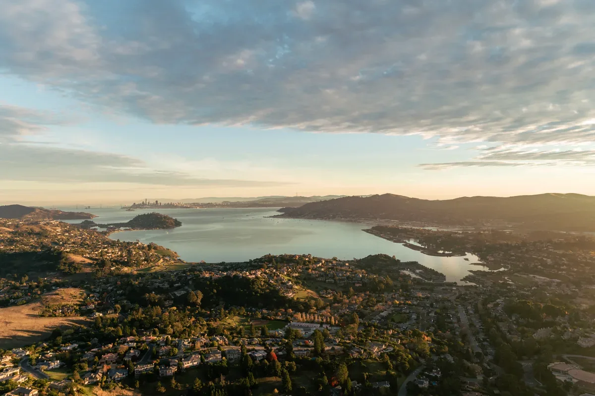 Vista aérea de un lago rodeado de casas y cerros al atardecer