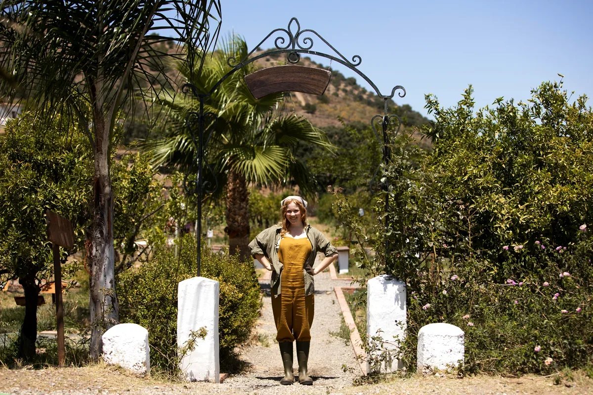 Mujer de pie a la entrada de un jardín con un arco de hierro y palmeras