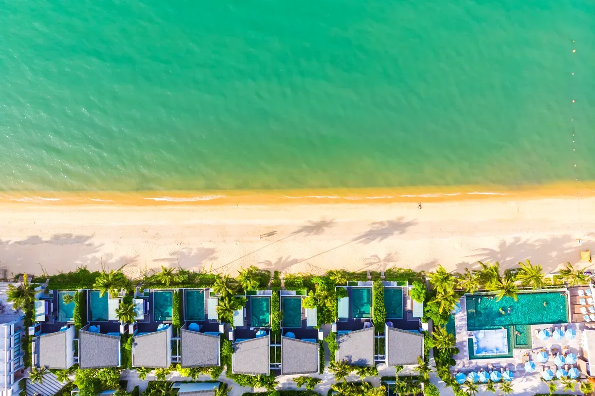 Vista cenital de una playa con hotel, albercas y mar verde turquesa