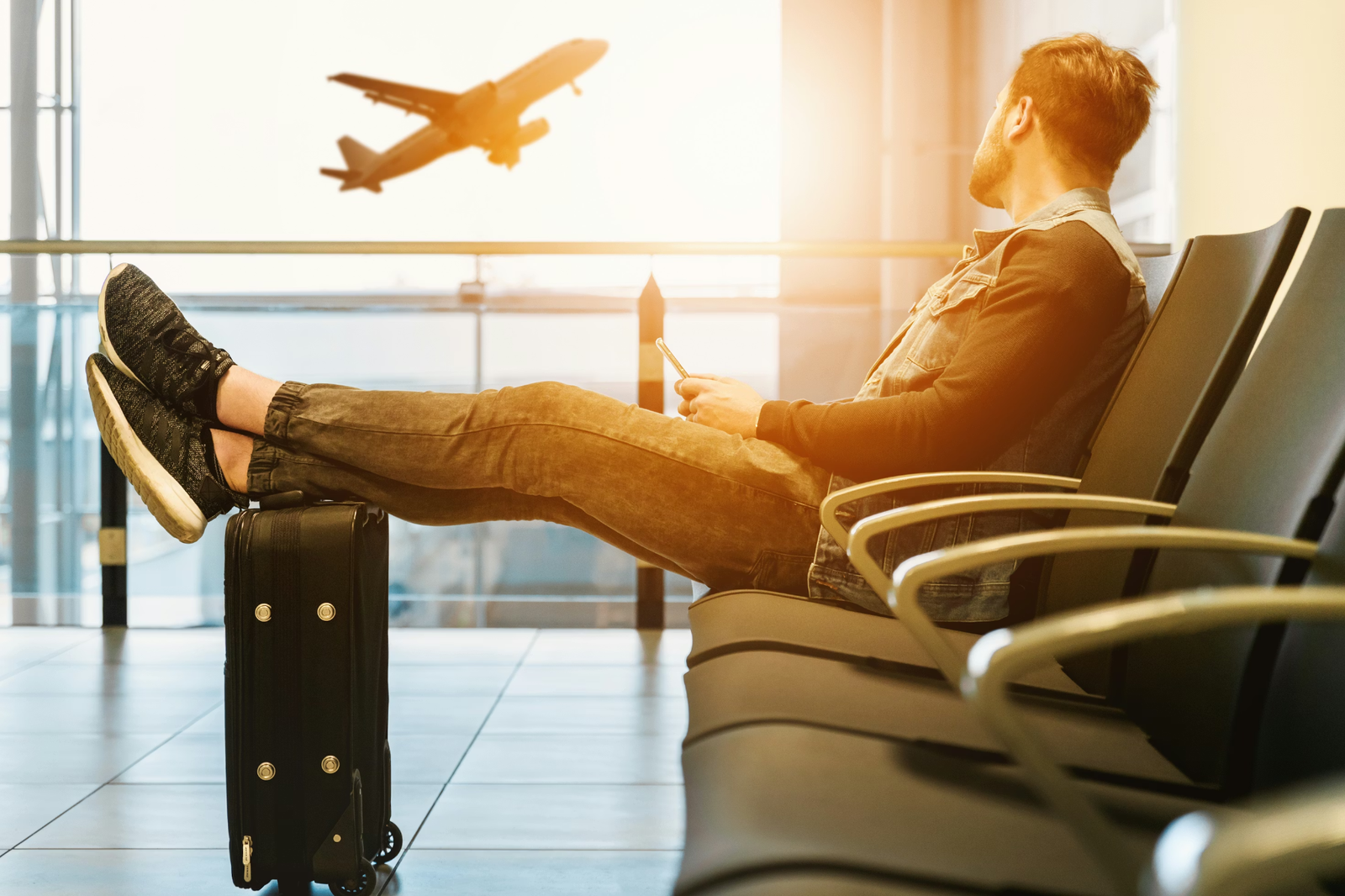 Hombre que espera su vuelo con los pies sobre la maleta mientras despega un avión