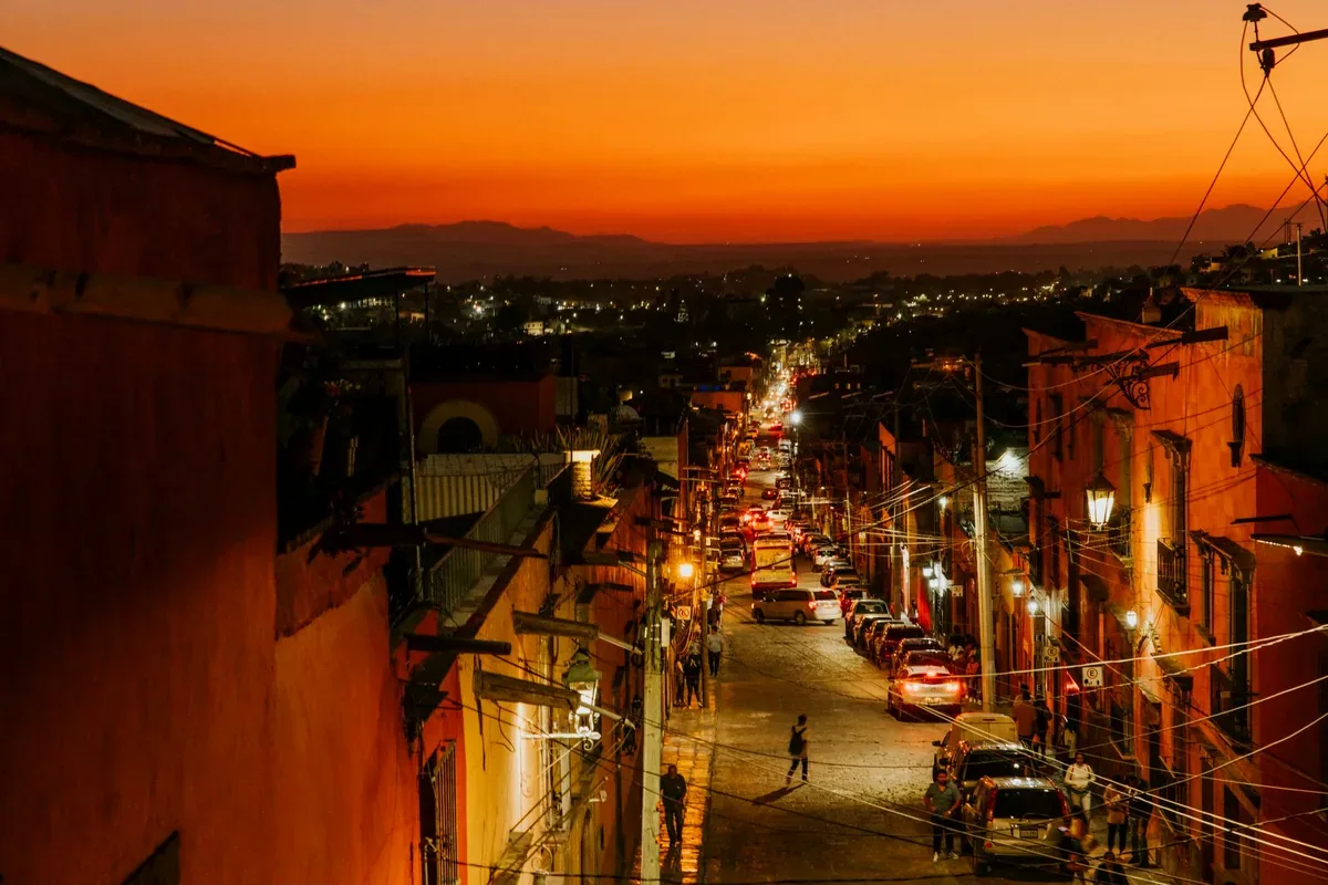 Calle de un centro histórico iluminada al atardecer con autos estacionados