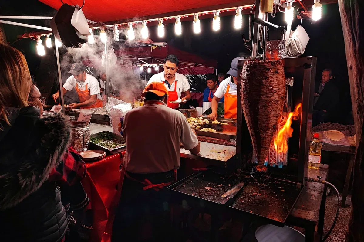 Taqueros preparando tacos al pastor junto al trompo en un puesto nocturno