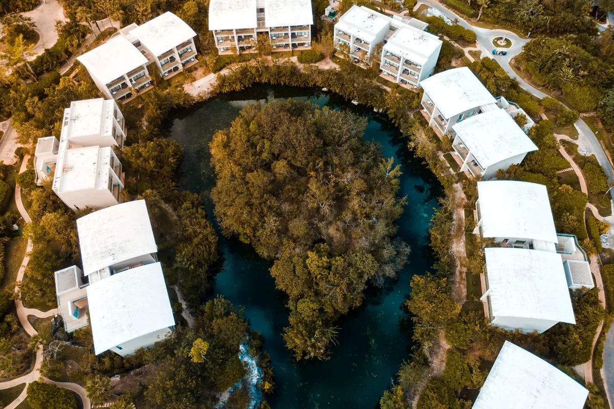 Vista aérea de casas blancas alrededor de un cenote en la selva