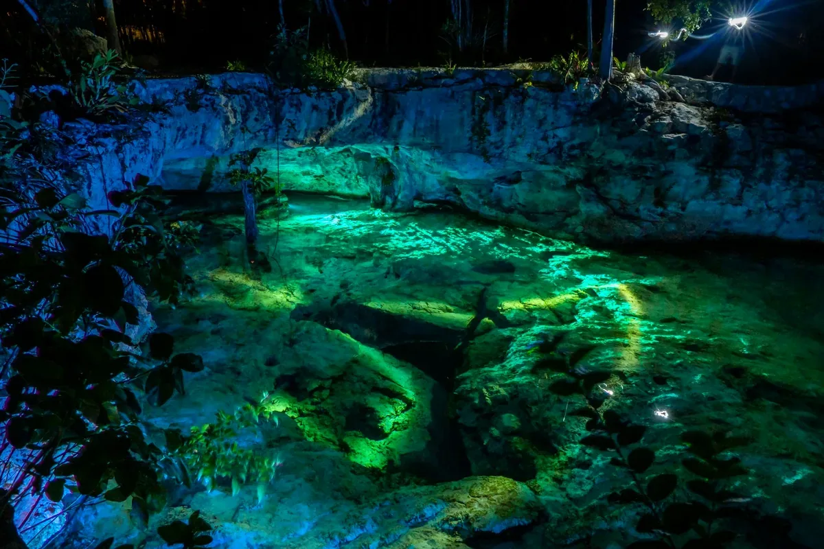 Cenote iluminado de noche con reflejos verdes y azules