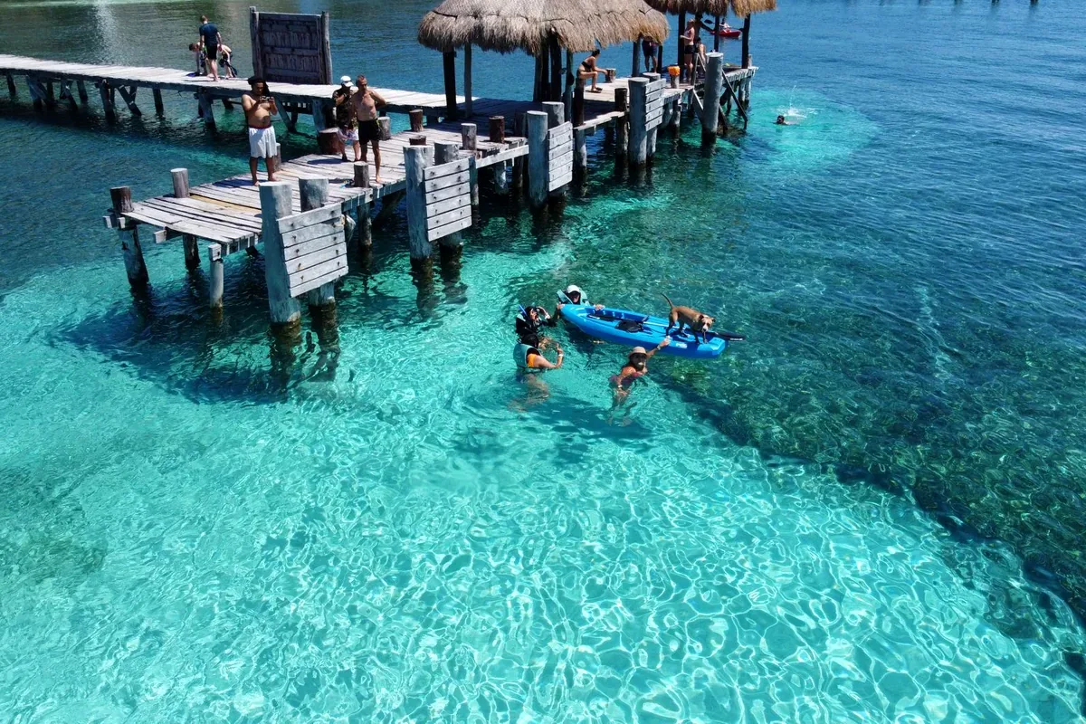 Muelle de madera sobre agua turquesa con bañistas y un kayak