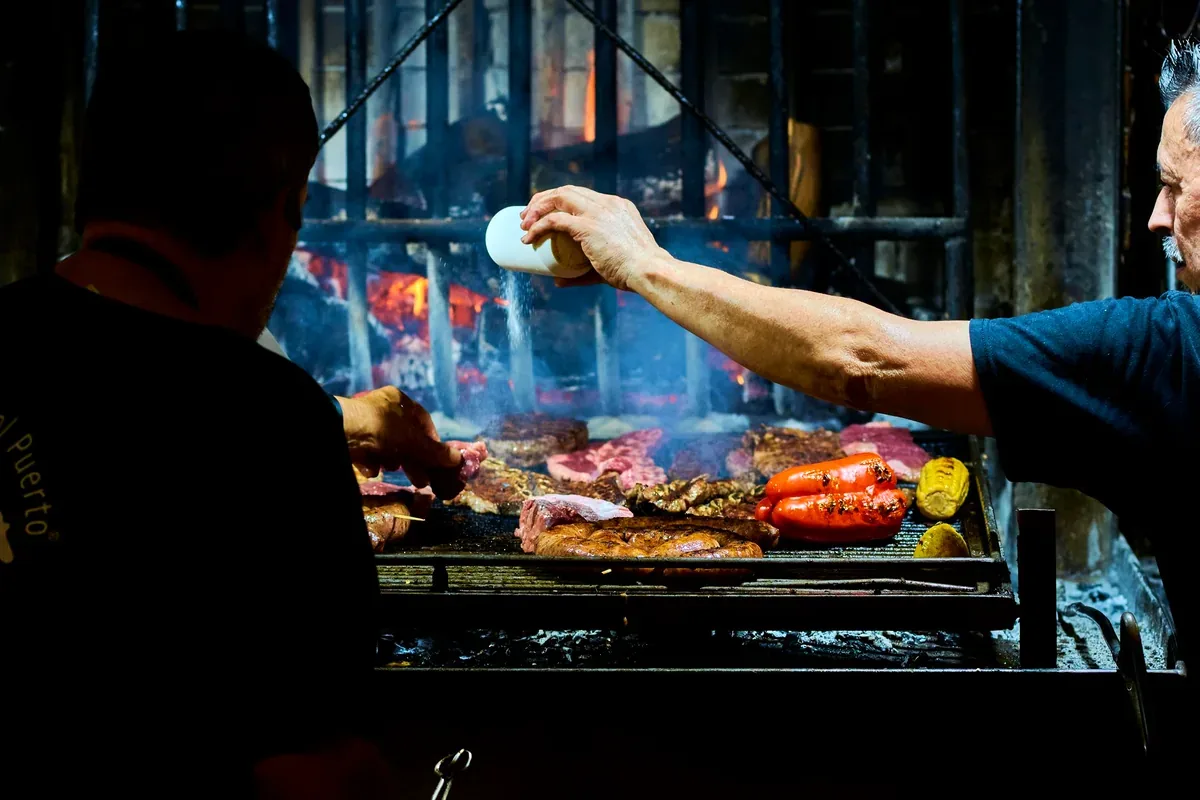 Parrillero que sala carnes y chorizos sobre una parrilla de leña
