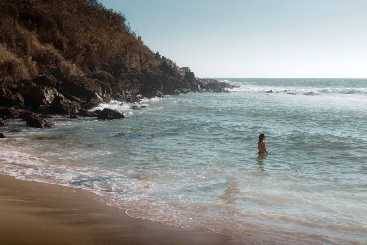 Bañista en el mar de una playa con cerros rocosos