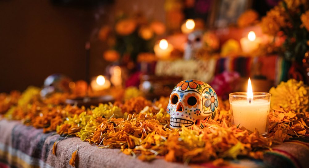 Ofrenda con flores de cempasúchil, una calavera pintada y una vela encendida