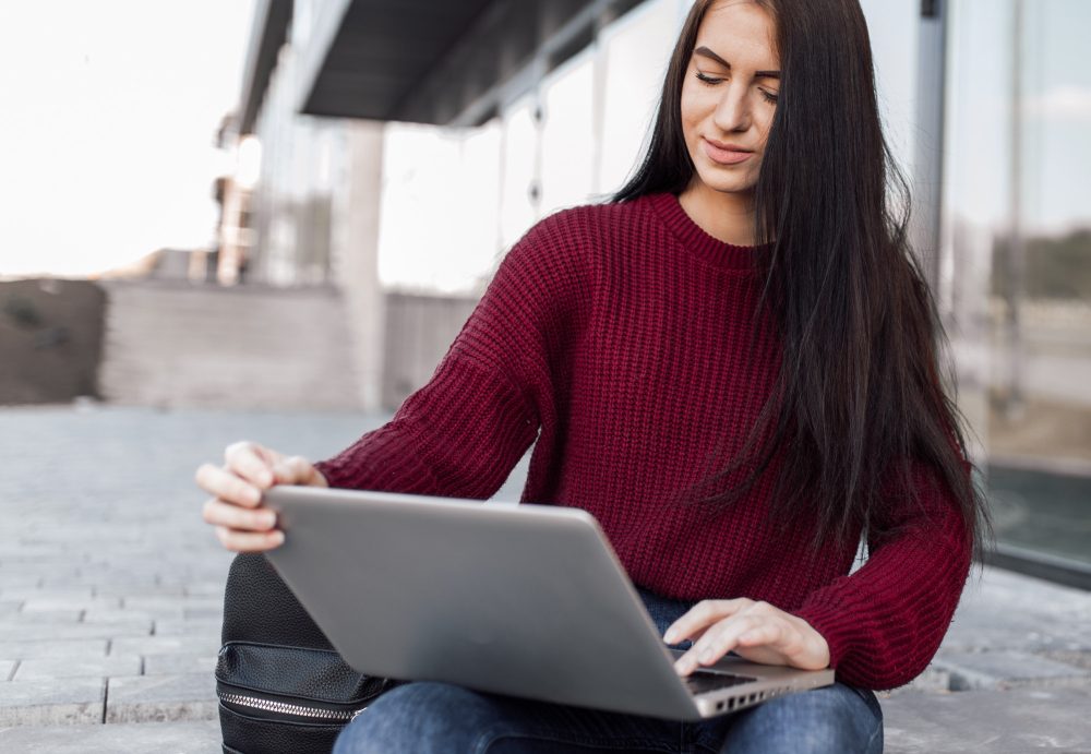 Joven sentada en la calle que trabaja en una laptop