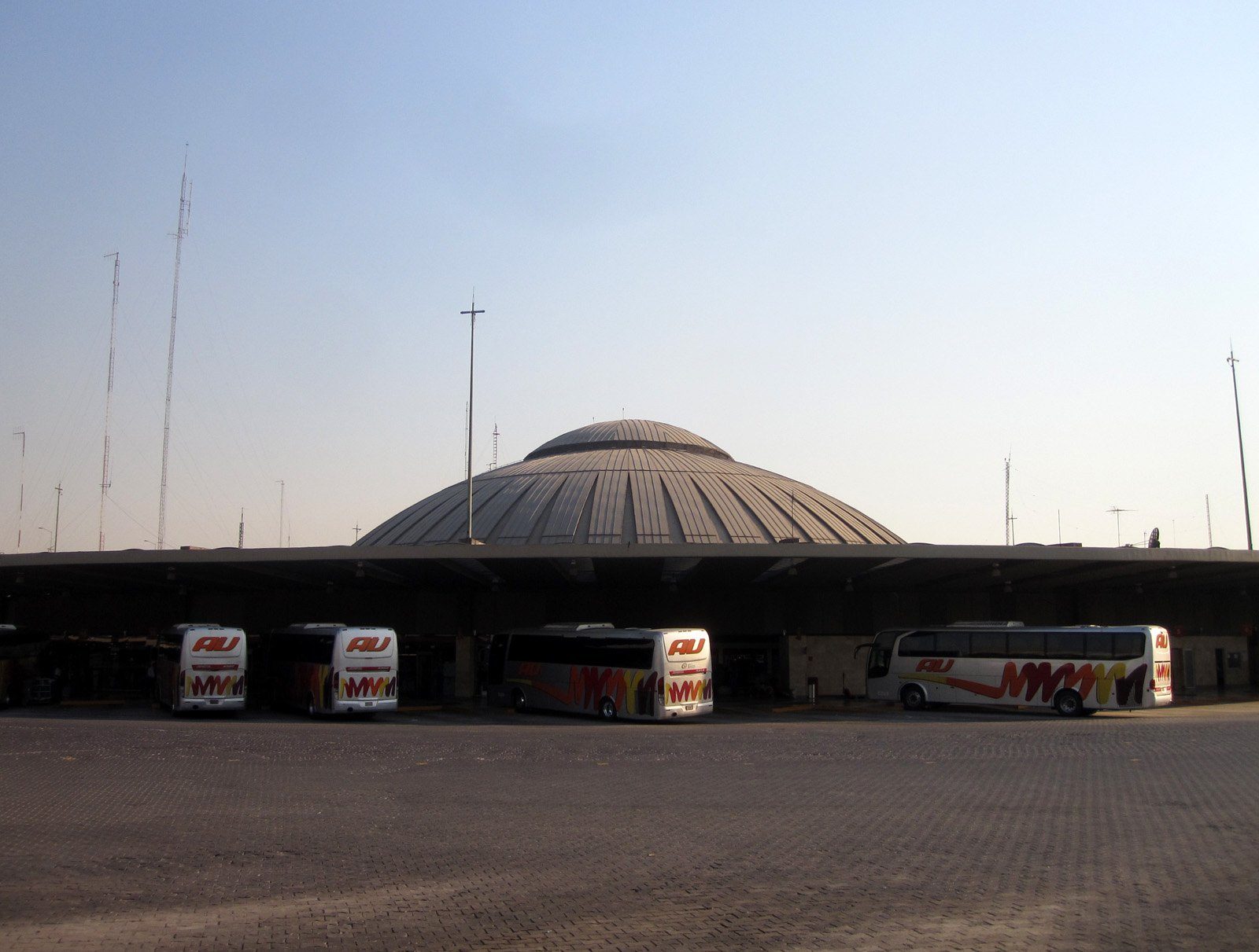 Cúpula de la terminal TAPO con varios autobuses ADO estacionados frente a la techumbre de los andenes