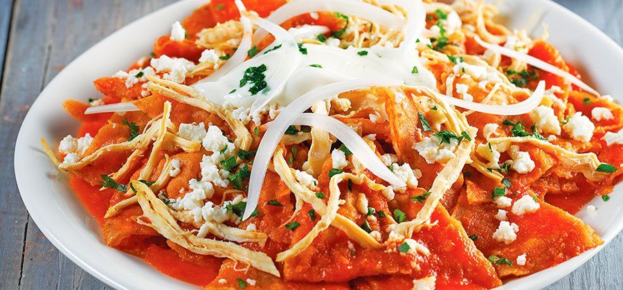 Plato de chilaquiles rojos con queso desmenuzado, crema, cebolla y cilantro sobre totopos bañados en salsa roja