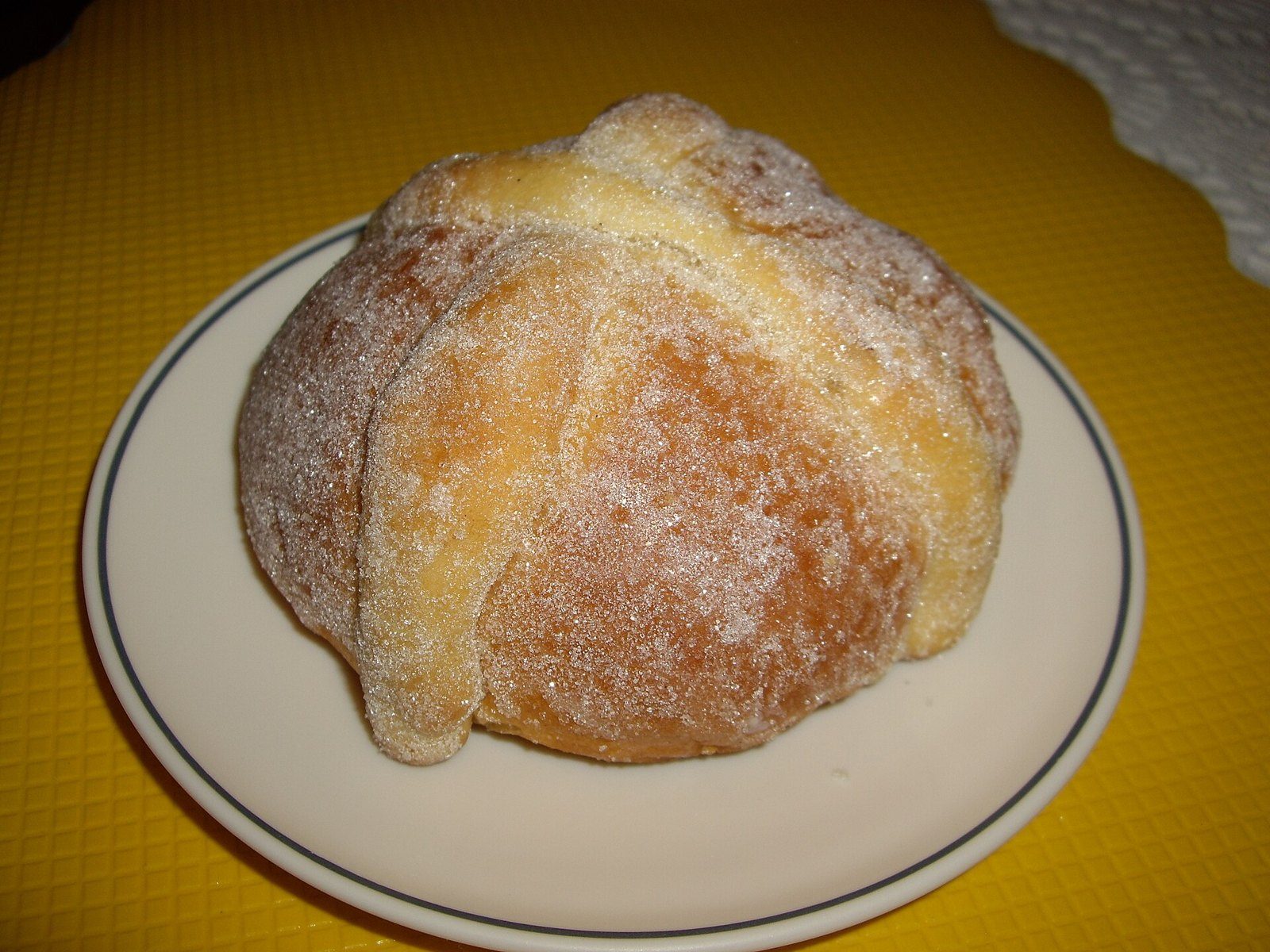 Pan de muerto con azúcar espolvoreada y tiras en forma de huesos, servido en un plato blanco