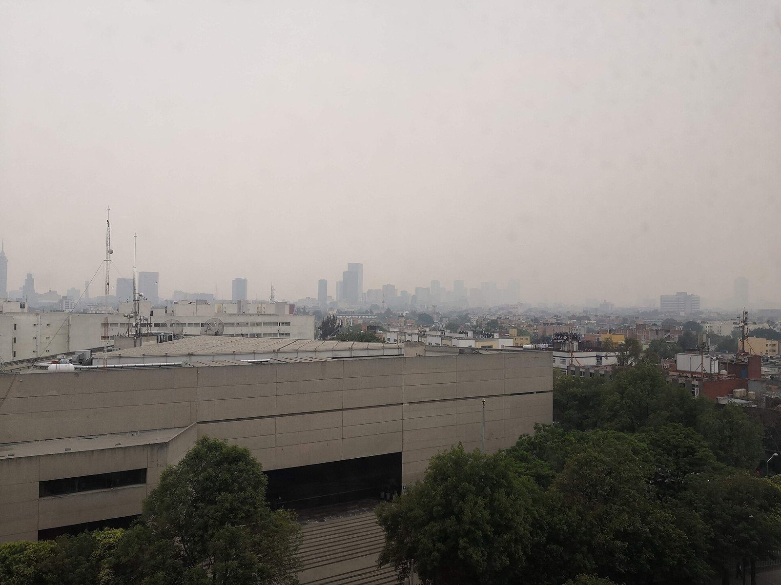 Vista de la Ciudad de México con el cielo cubierto de una capa gris de contaminación, edificios en primer plano y rascacielos al fondo