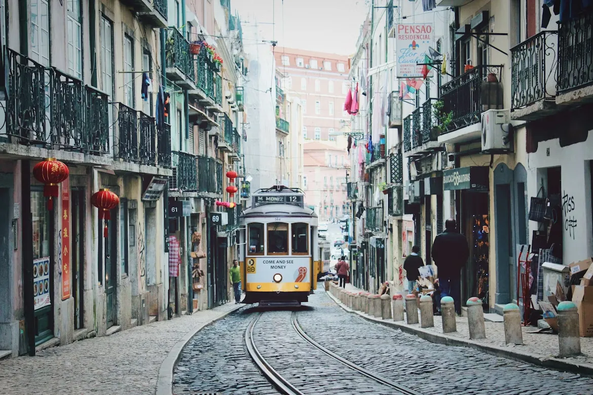 Tranvía amarillo por una calle empedrada del centro de Lisboa, entre edificios con balcones de hierro