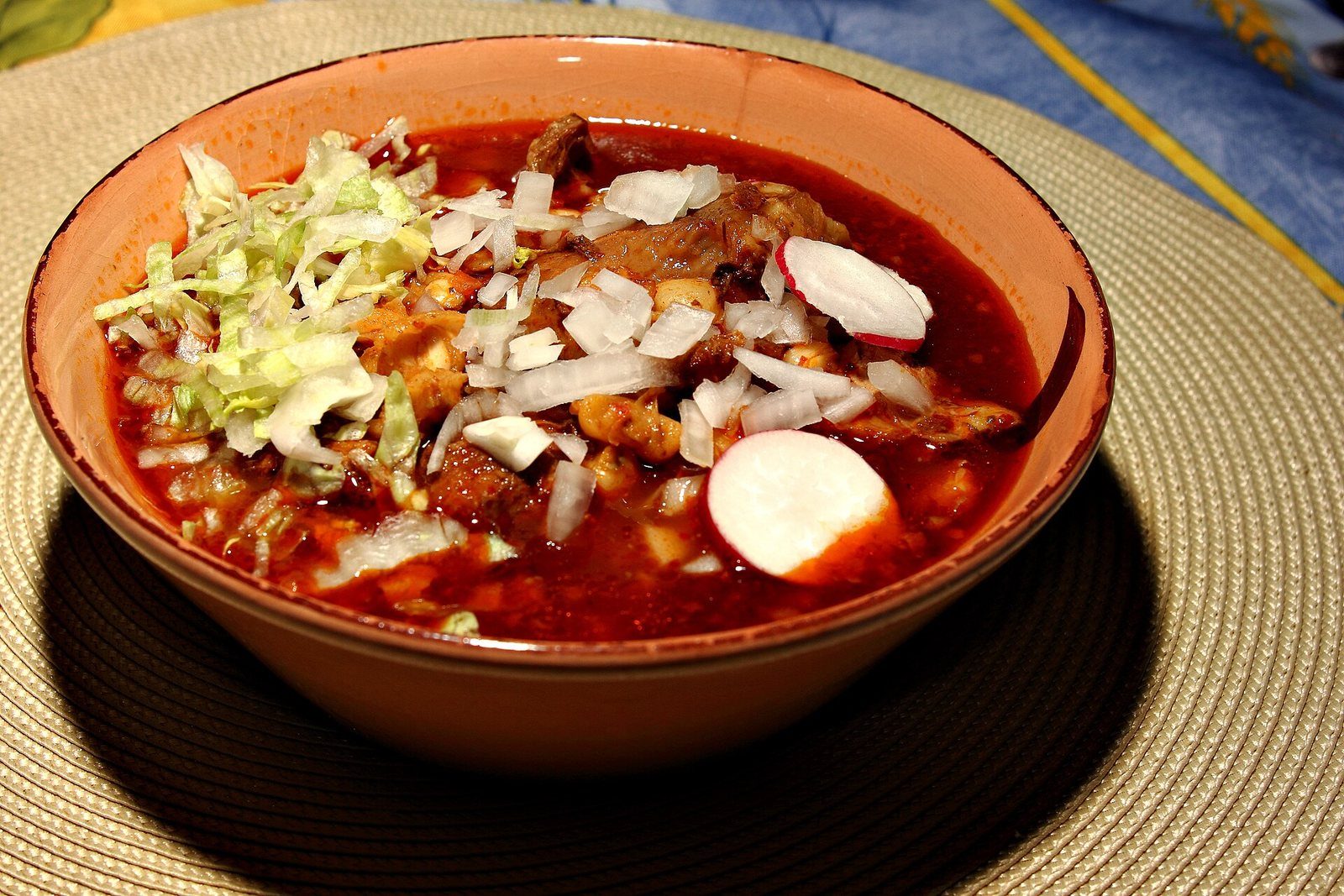 Plato hondo de pozole rojo con carne, cebolla picada, lechuga y rodajas de rábano