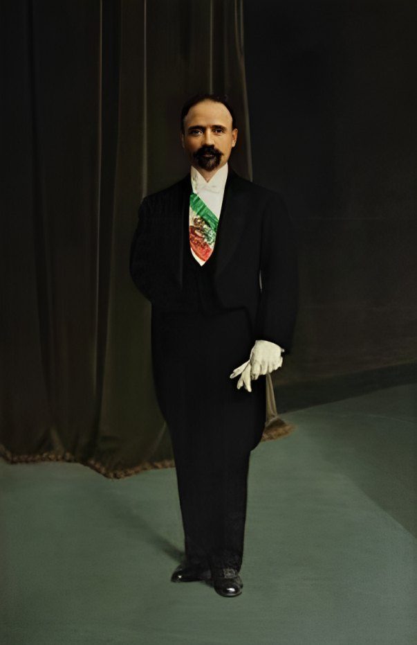 Retrato de cuerpo completo de Francisco I. Madero con traje oscuro, guante blanco y banda presidencial, frente a una cortina